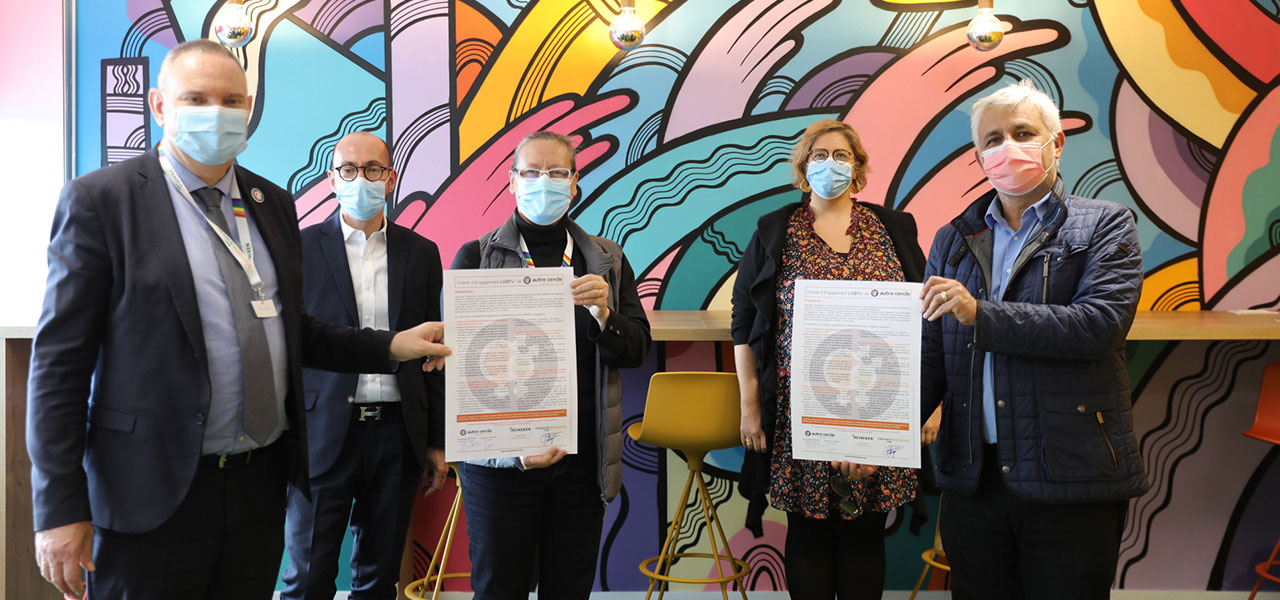 banniere_signature Quatre personnes masquées tenant des documents devant une fresque murale colorée lors d'une rencontre officielle.